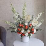 A vase containing delphiniums, anthuriums, roses and carnations by Novo